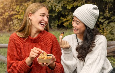 Zwei junge Frauen genießen im Park Churrini aus einer To-Go-verpackung mit einem schokoladigen Dip.